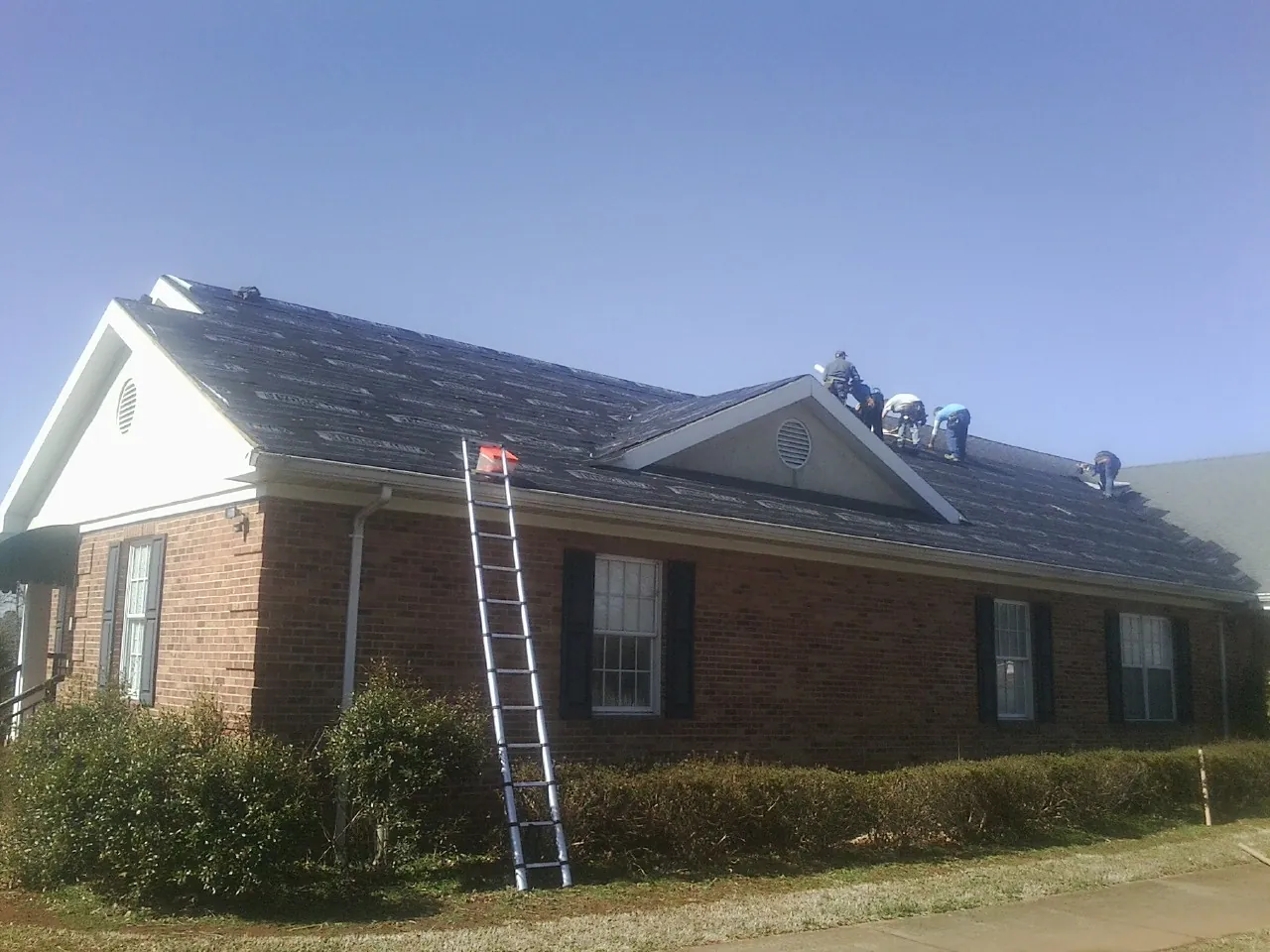 Crew tearing shingles off a brick ranch roof with a ladder set — Emergency Roof Repair work by our crew in Pandora