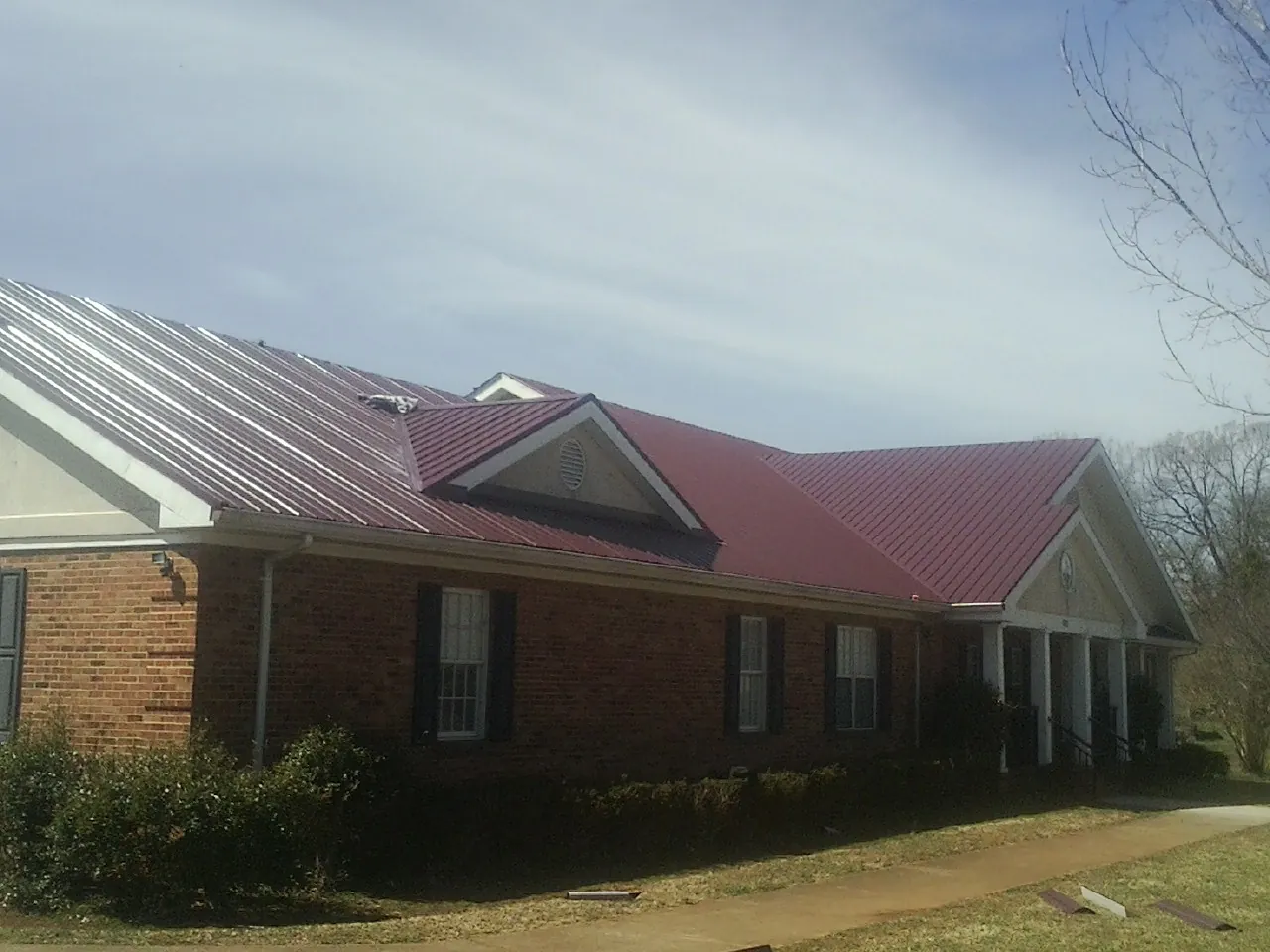 Red metal roof with gabled entries on a long brick building, from a Hail Damage Roof Repair job in Pandora