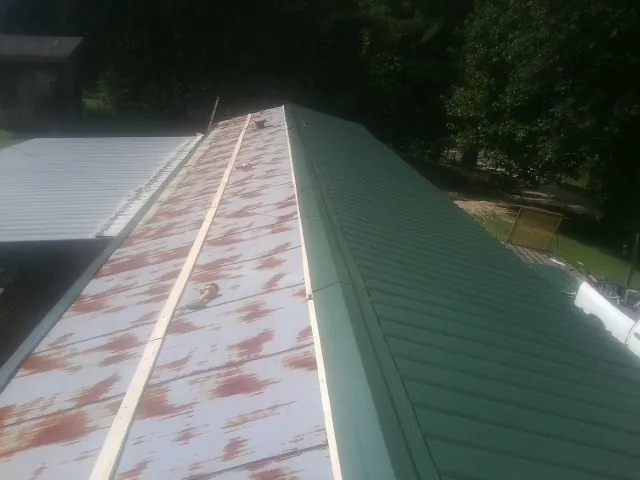 Old rusted panels beside newly installed green metal roofing — Wind Damage Roof Repair by Roofing Brothers in Pandora